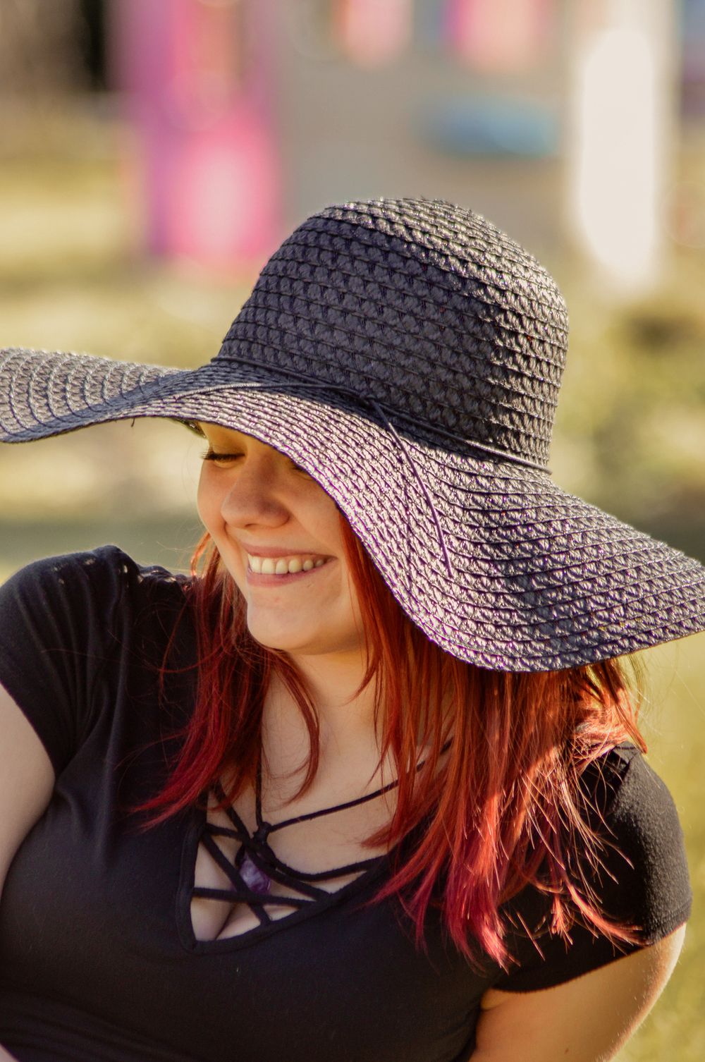 A person wearing a wide-brimmed black sun hat and black top smiles while posing outdoors in natural lighting.