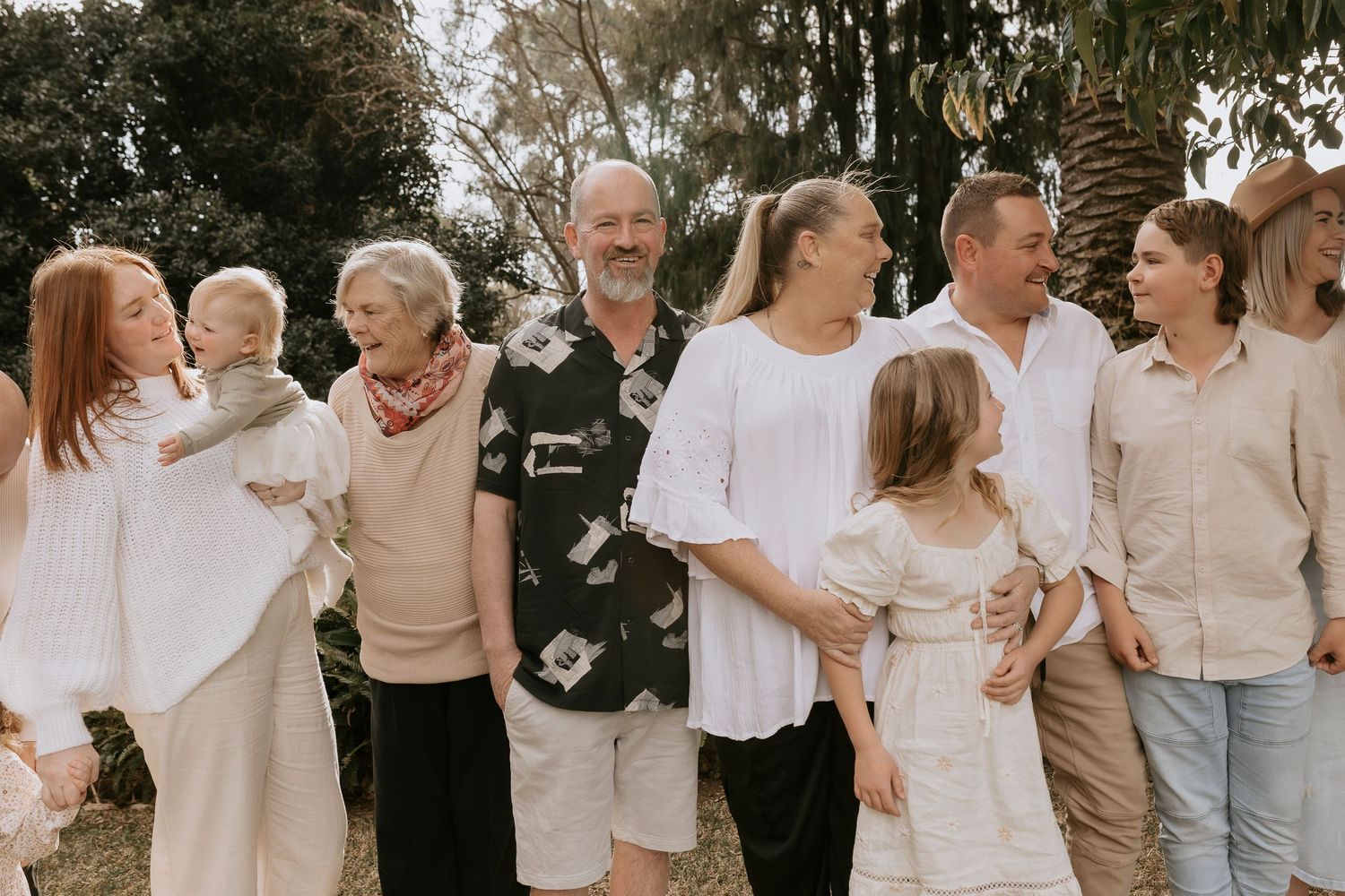 A group wearing coordinated neutral beige and white outfits laughs together during an outdoor photo session.