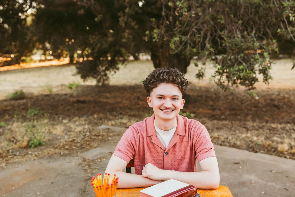 A person sits at a wooden table outdoors with orange pumpkins and fall decor during autumn season.