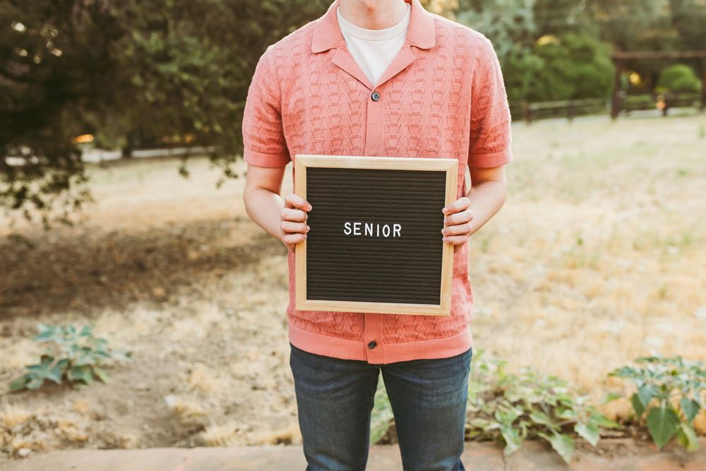 Person in coral shirt holding a chalkboard sign outdoors during golden hour.