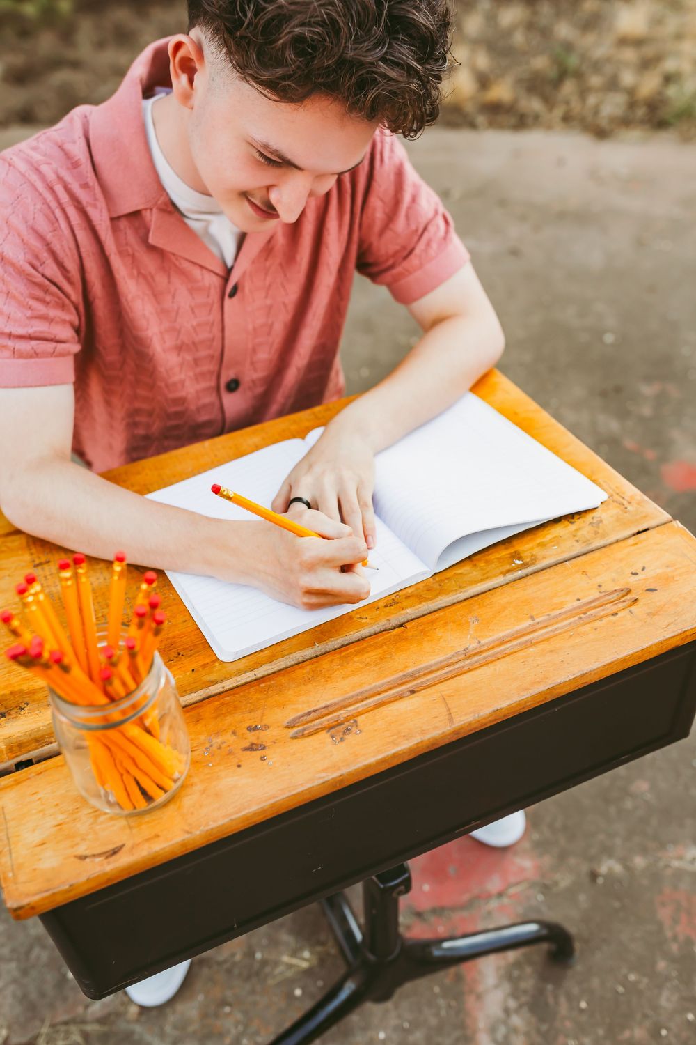 Student writing at an old-style wooden school desk with orange details in natural lighting.