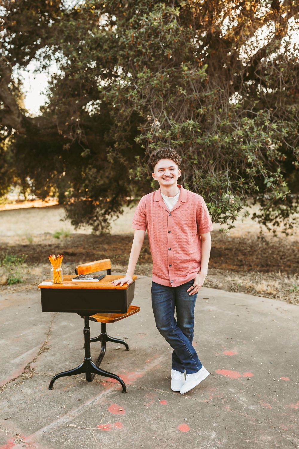 Person in coral shirt stands near orange school supplies on outdoor table at sunset.