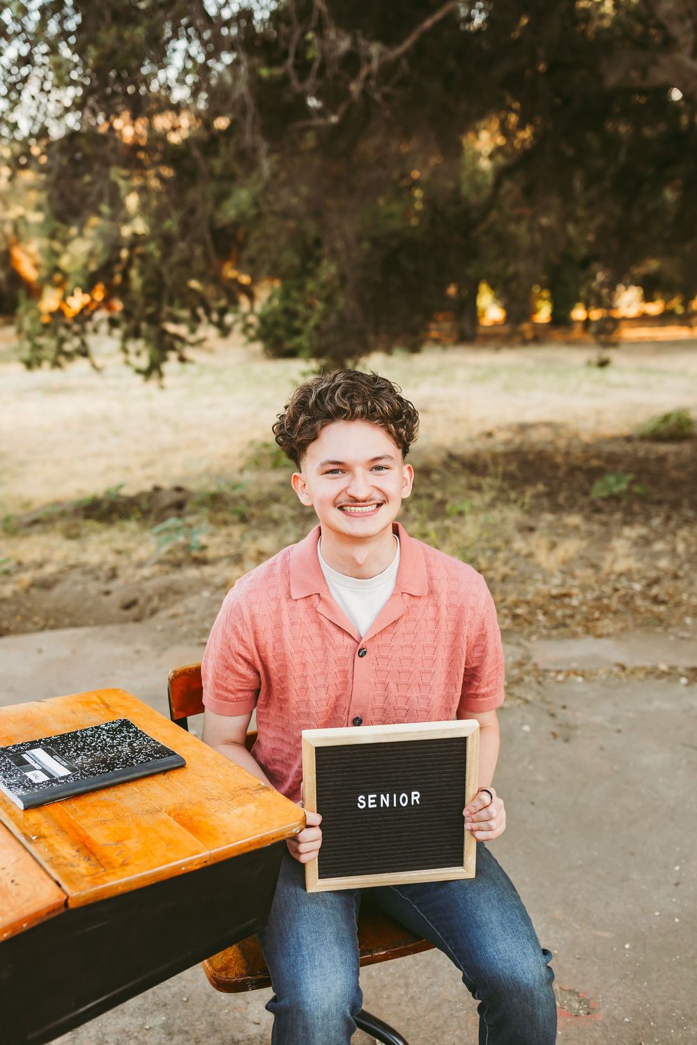 Senior photo session outdoors featuring casual attire and a small chalkboard sign at sunset.