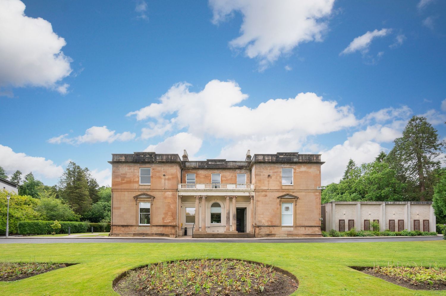 Modern brick building exterior with landscaped grounds under blue sky with white clouds.