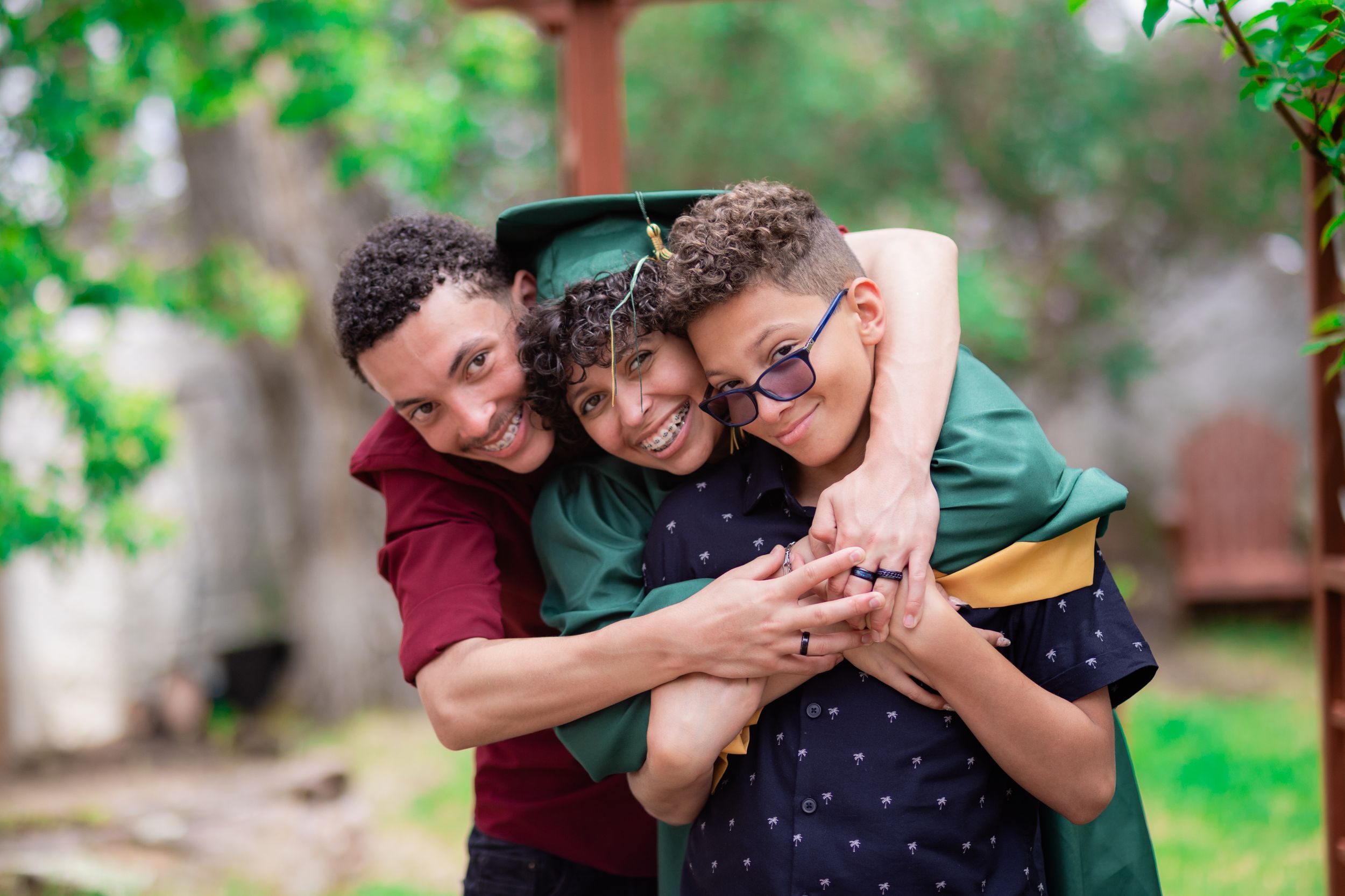 Three people sharing warm group hug and laughter in garden setting.