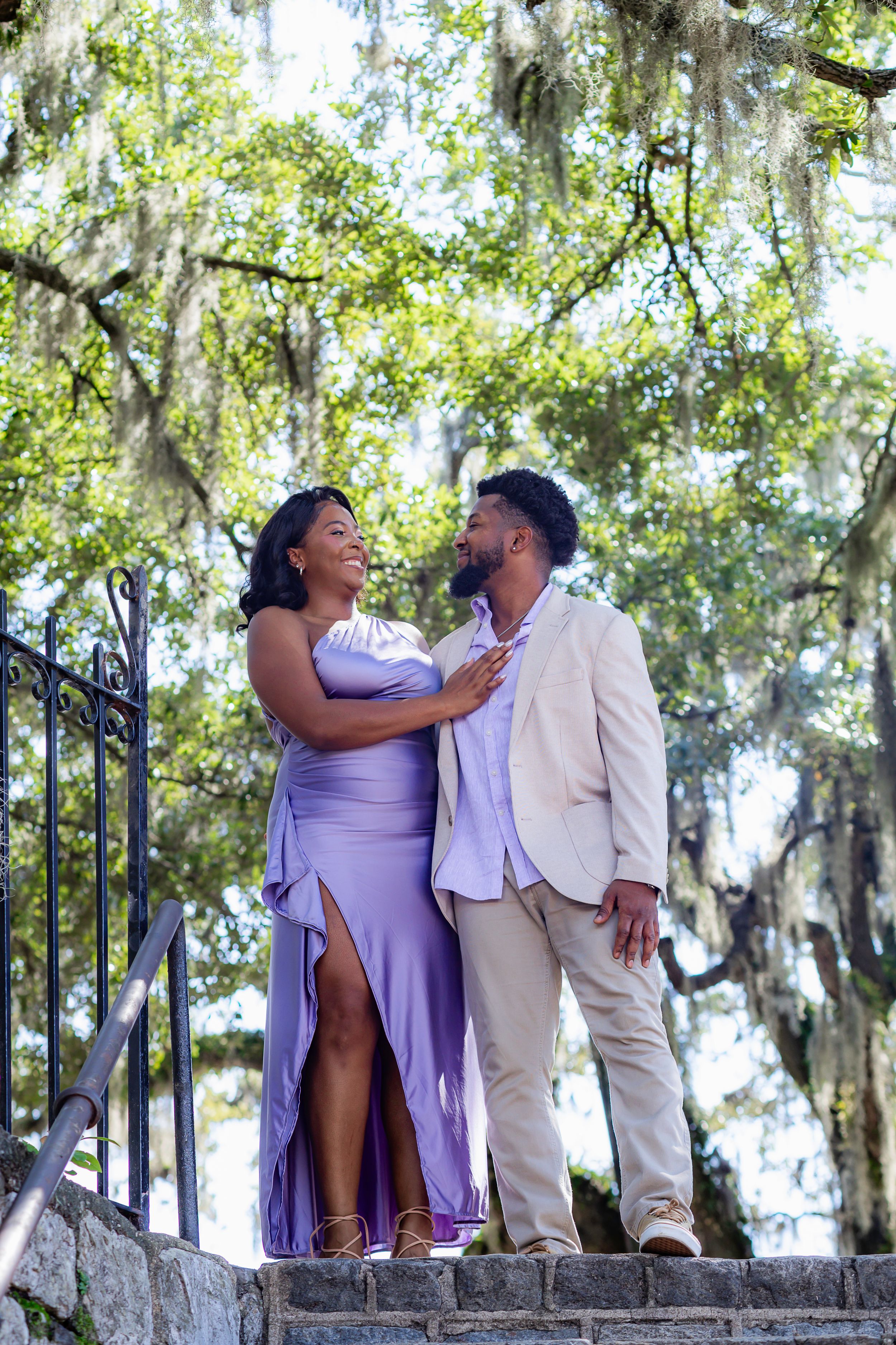 Couple shares romantic moment on stone steps surrounded by Spanish moss draped trees in a dreamy outdoor setting.