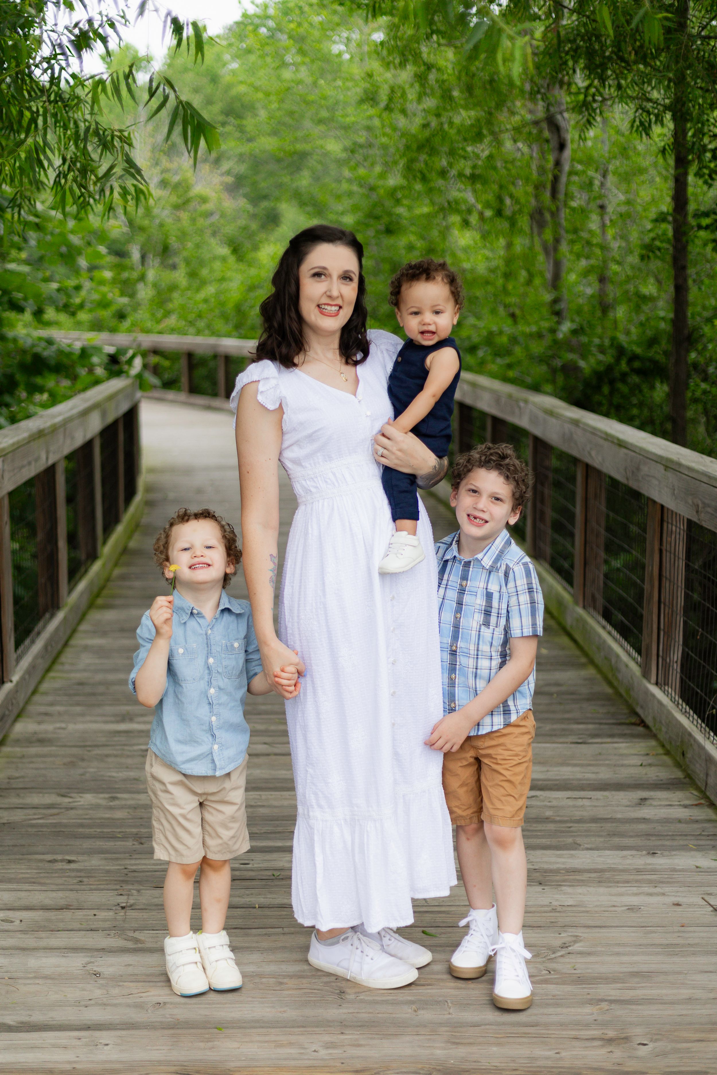 Family group poses together on wooden boardwalk surrounded by lush greenery.