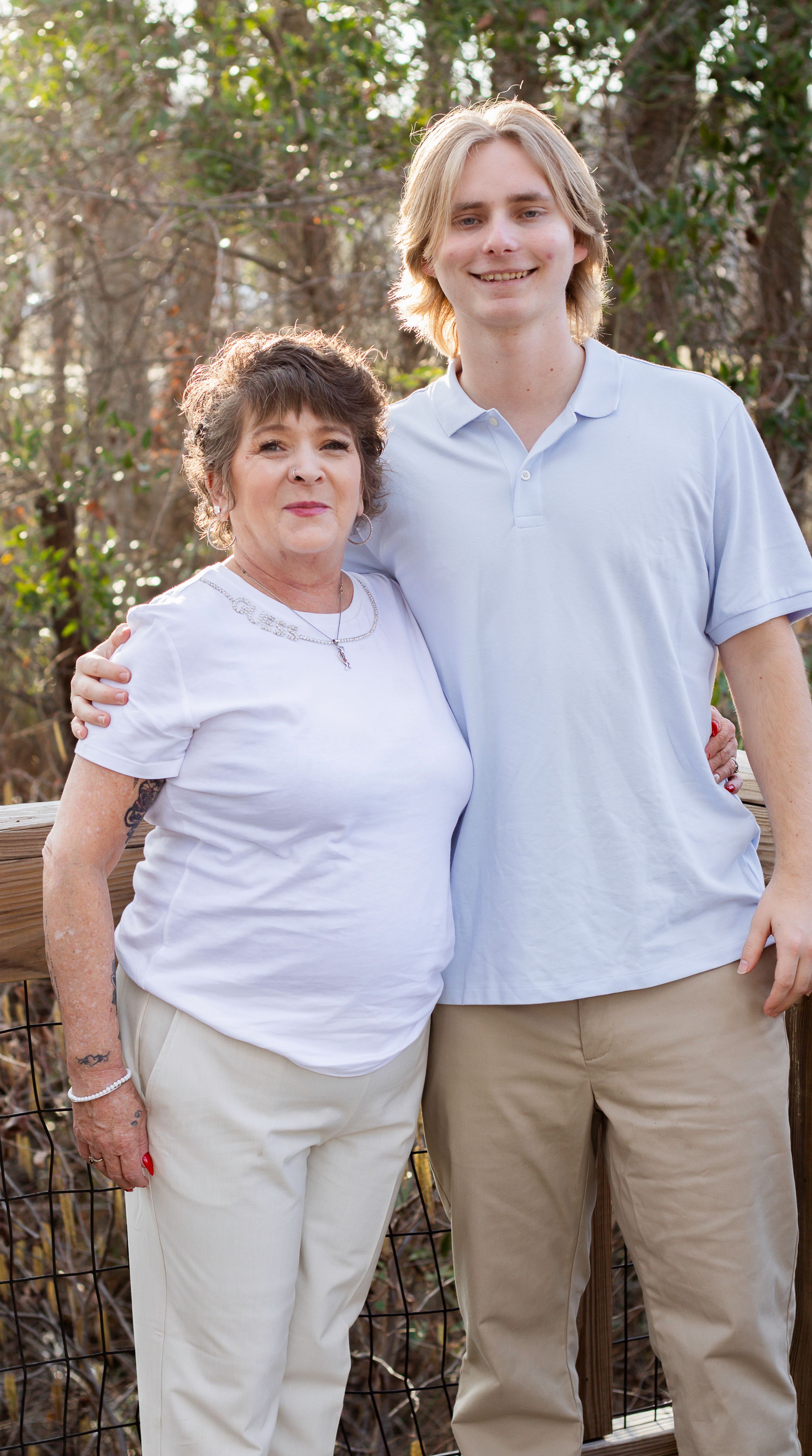 Two people in white polo shirts pose together outdoors against iron fence.