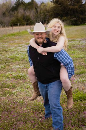 Playful couple in casual wear share affectionate moments in outdoor field setting.