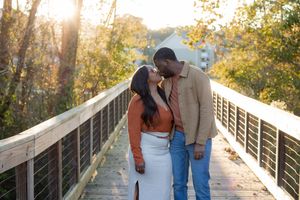 A couple shares a romantic moment on a wooden bridge surrounded by autumn foliage and golden sunlight.