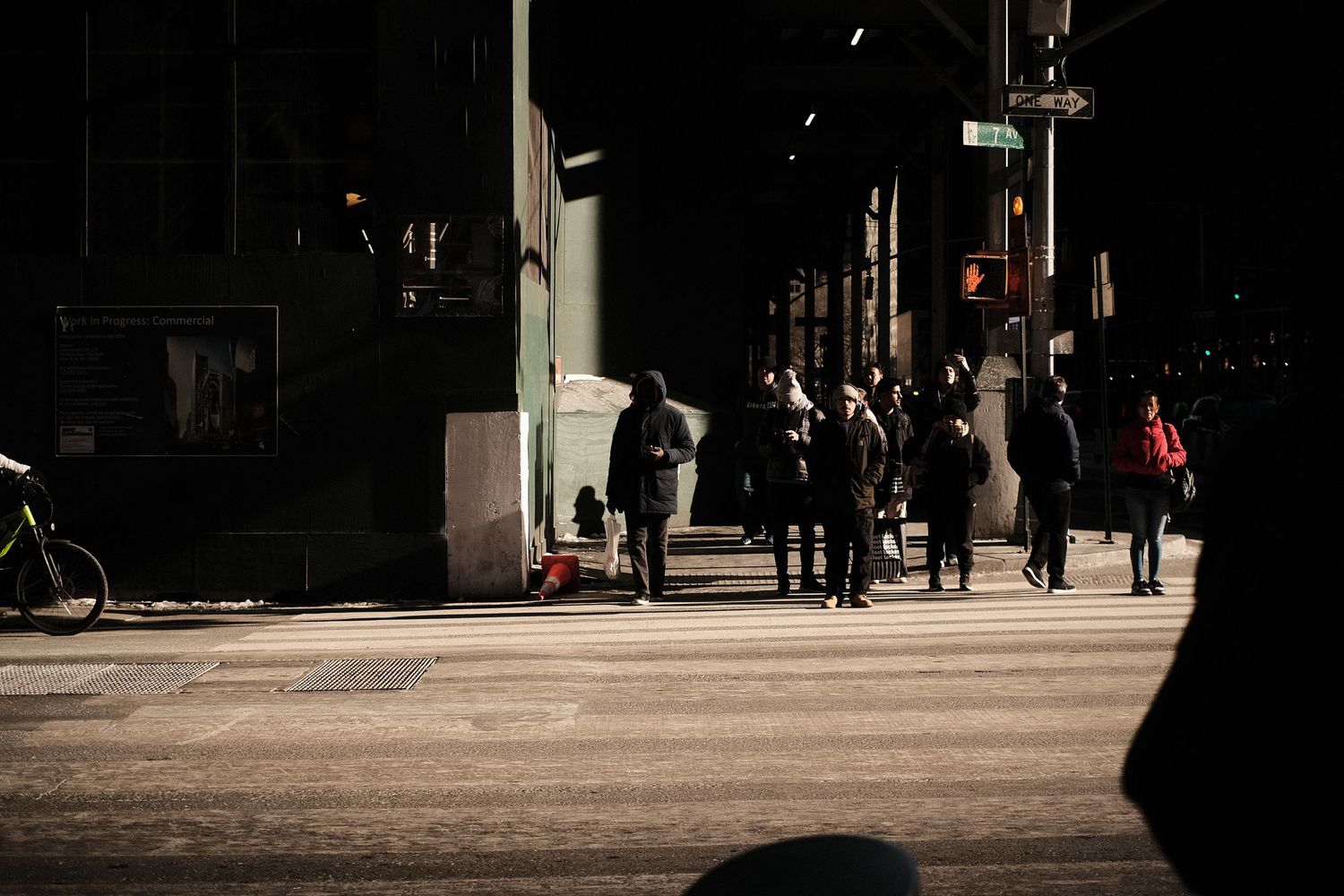 Dark urban walkway with silhouettes of people moving through shadows and light.