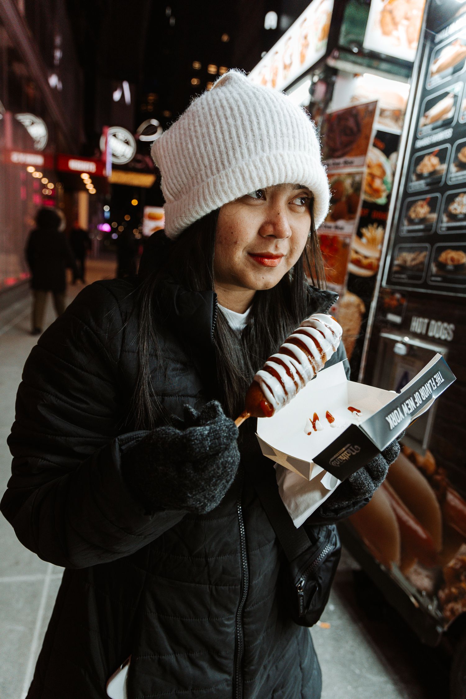 Person in winter attire enjoying food at an outdoor venue.