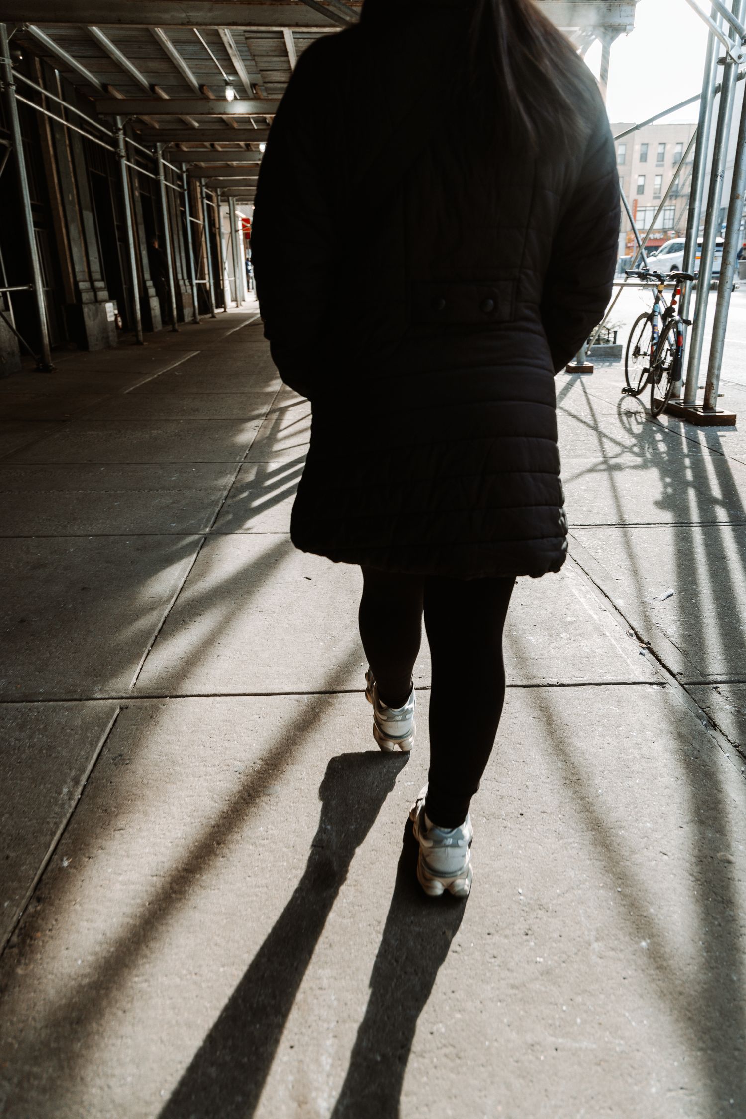 Shadow silhouette of someone walking on a covered urban sidewalk.