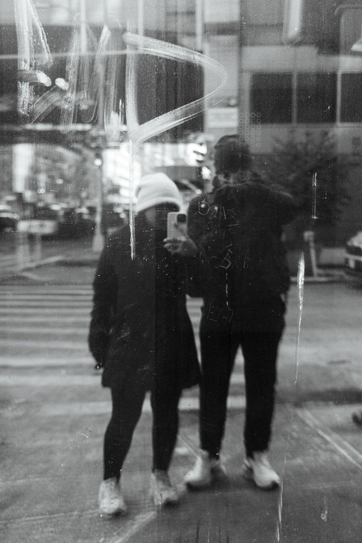 Black and white street photograph showing silhouettes of people through reflective glass.