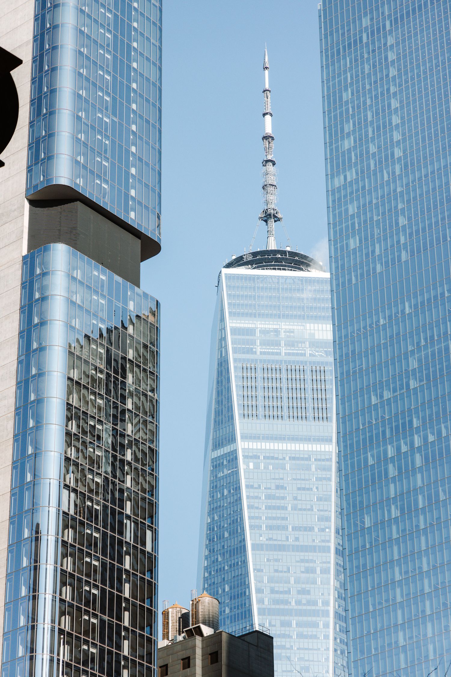 Modern glass skyscrapers reflecting sunlight against a blue sky with the Freedom Tower visible.