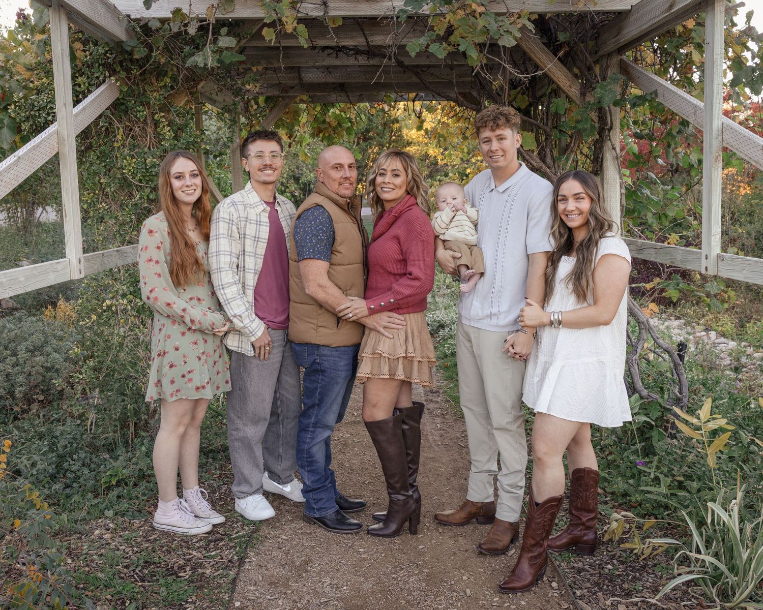 A group of people pose together under a wooden pergola in a garden setting during golden hour.