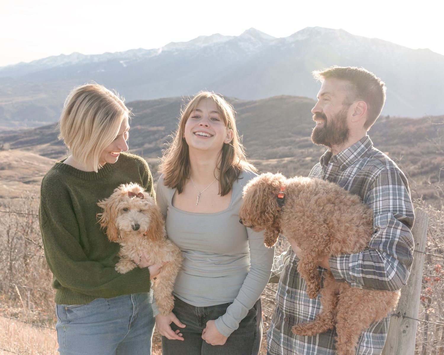 A group poses with their goldendoodle dog against a scenic mountain landscape during golden hour.