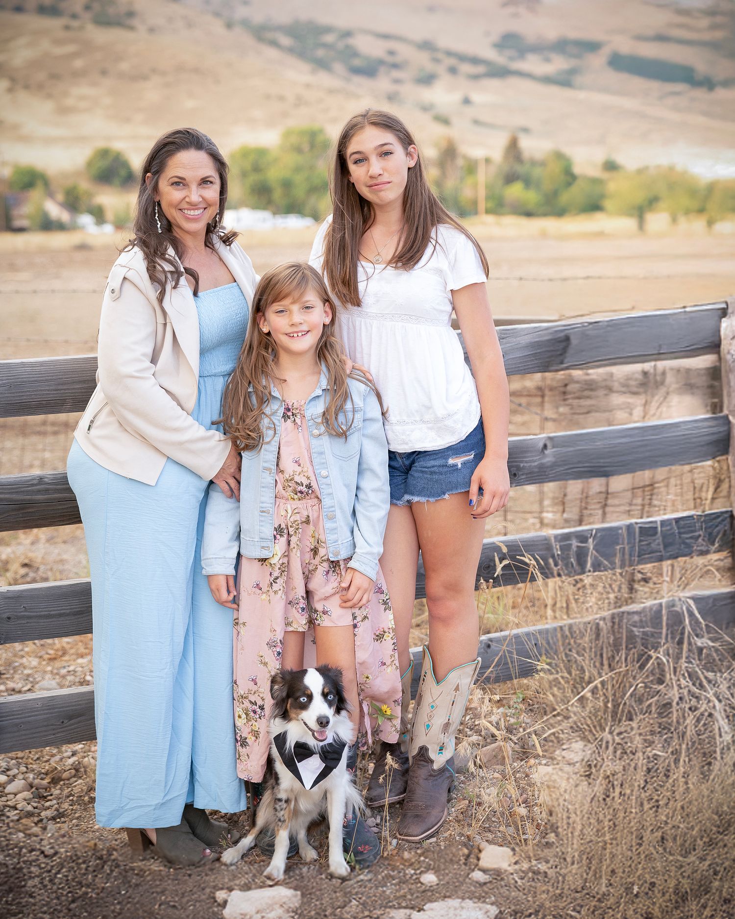 Family and dog posing together by a wooden fence in casual country attire.