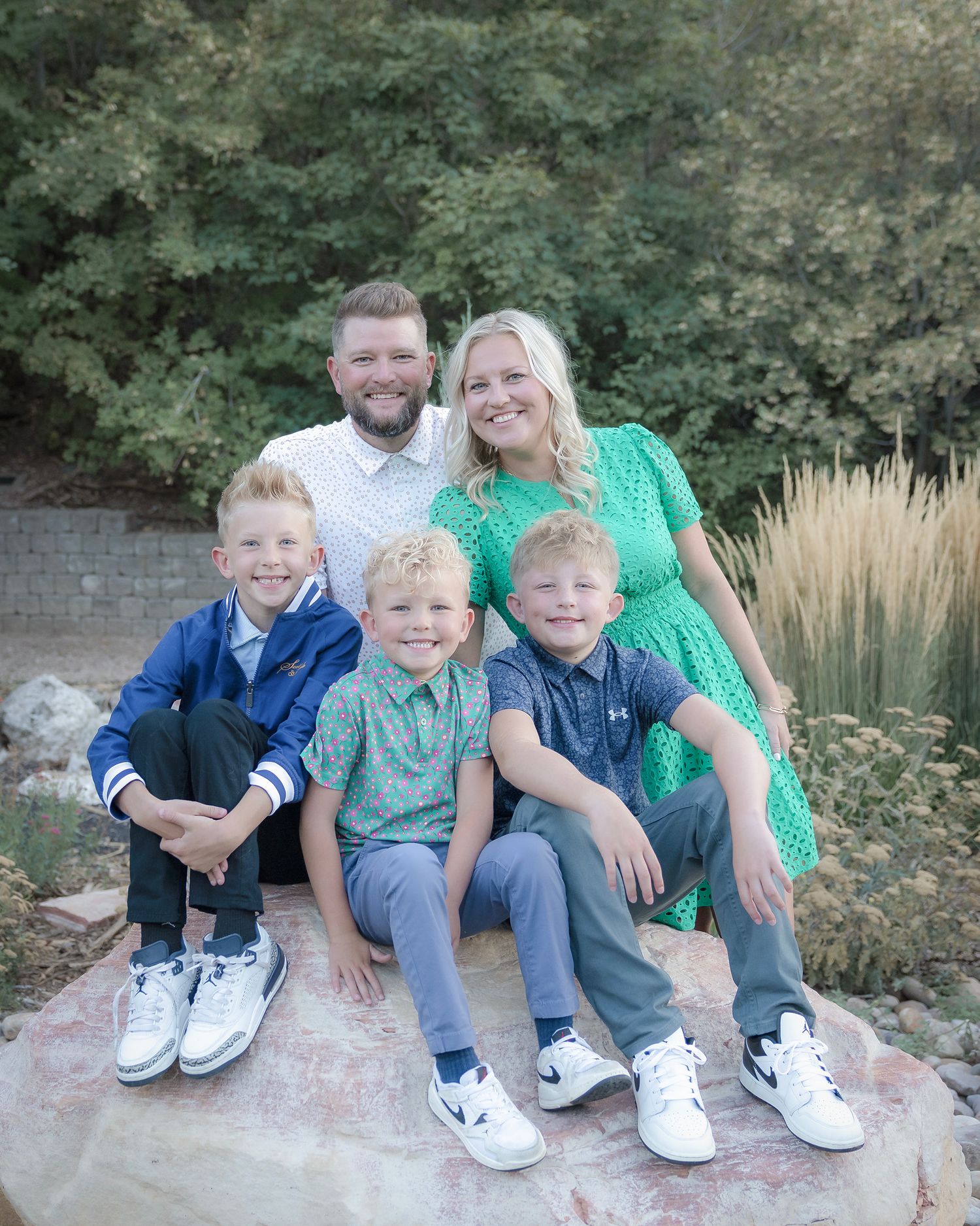 A family in coordinated blue and green outfits sits together on stone steps during an outdoor photo session.