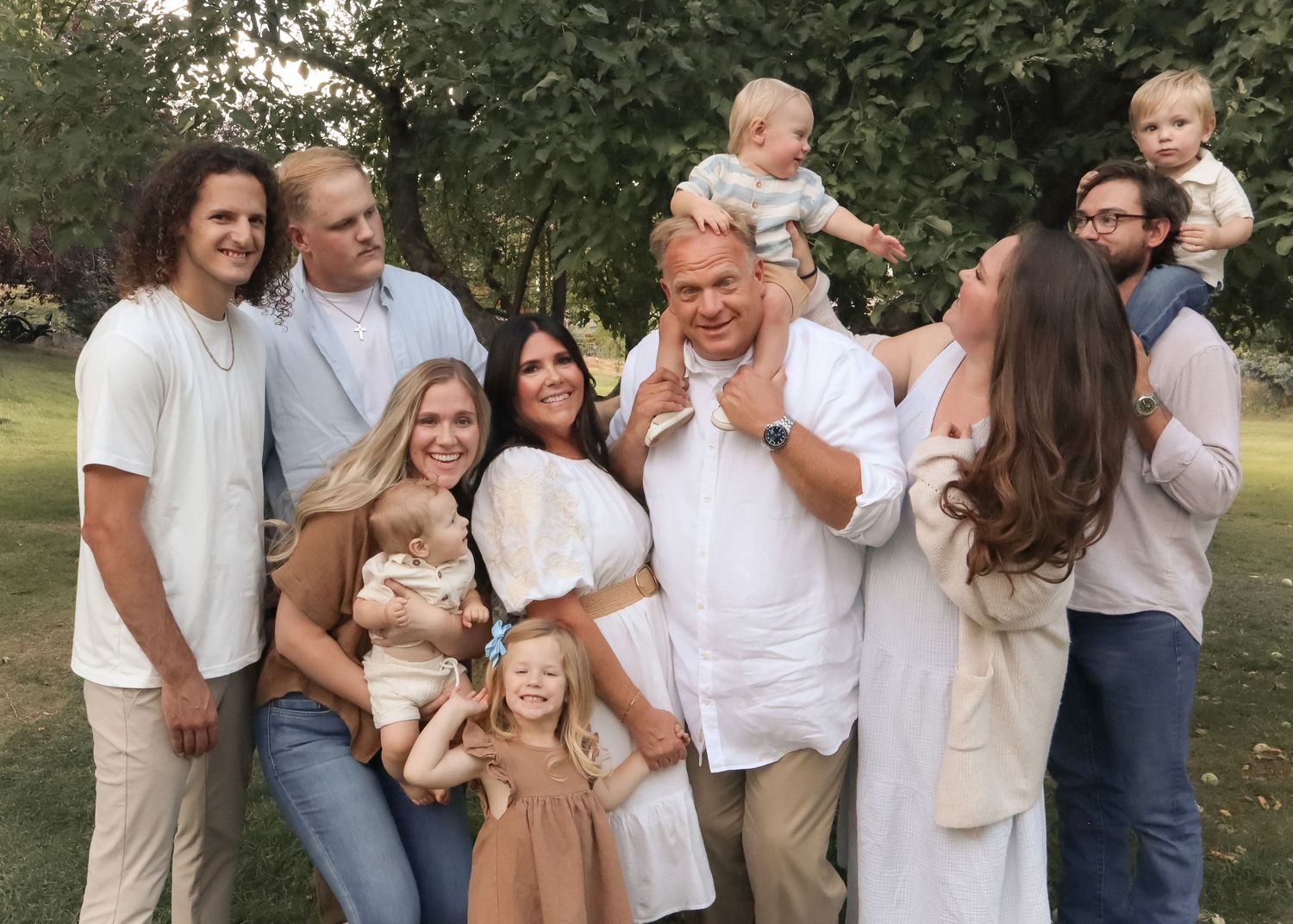 Large Family portrait with parents, adult children, and young kids smiling together outdoors in Ogden, Utah during a summer photo shoot.