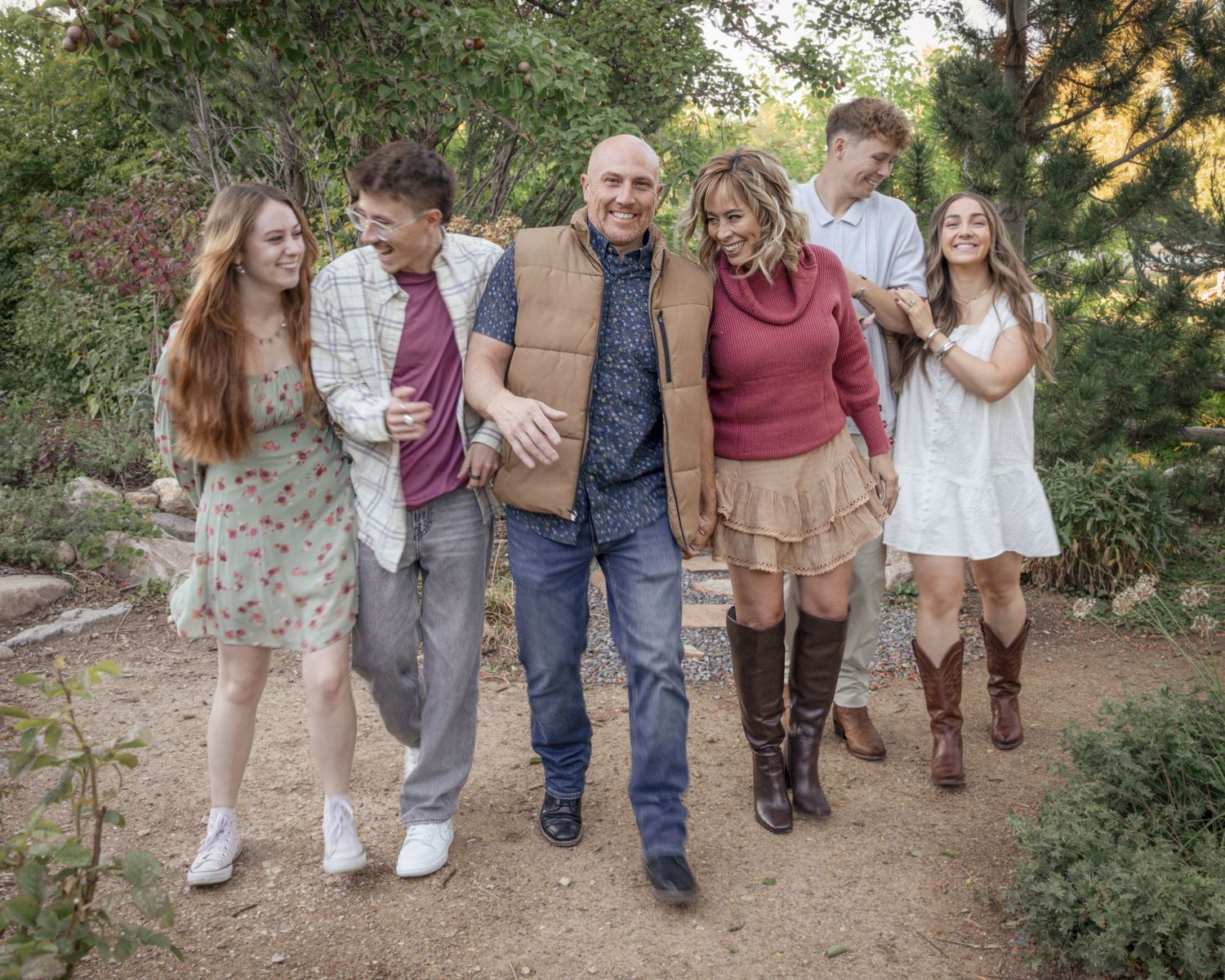 A group of five people walking together and laughing on a dirt path through a garden setting.