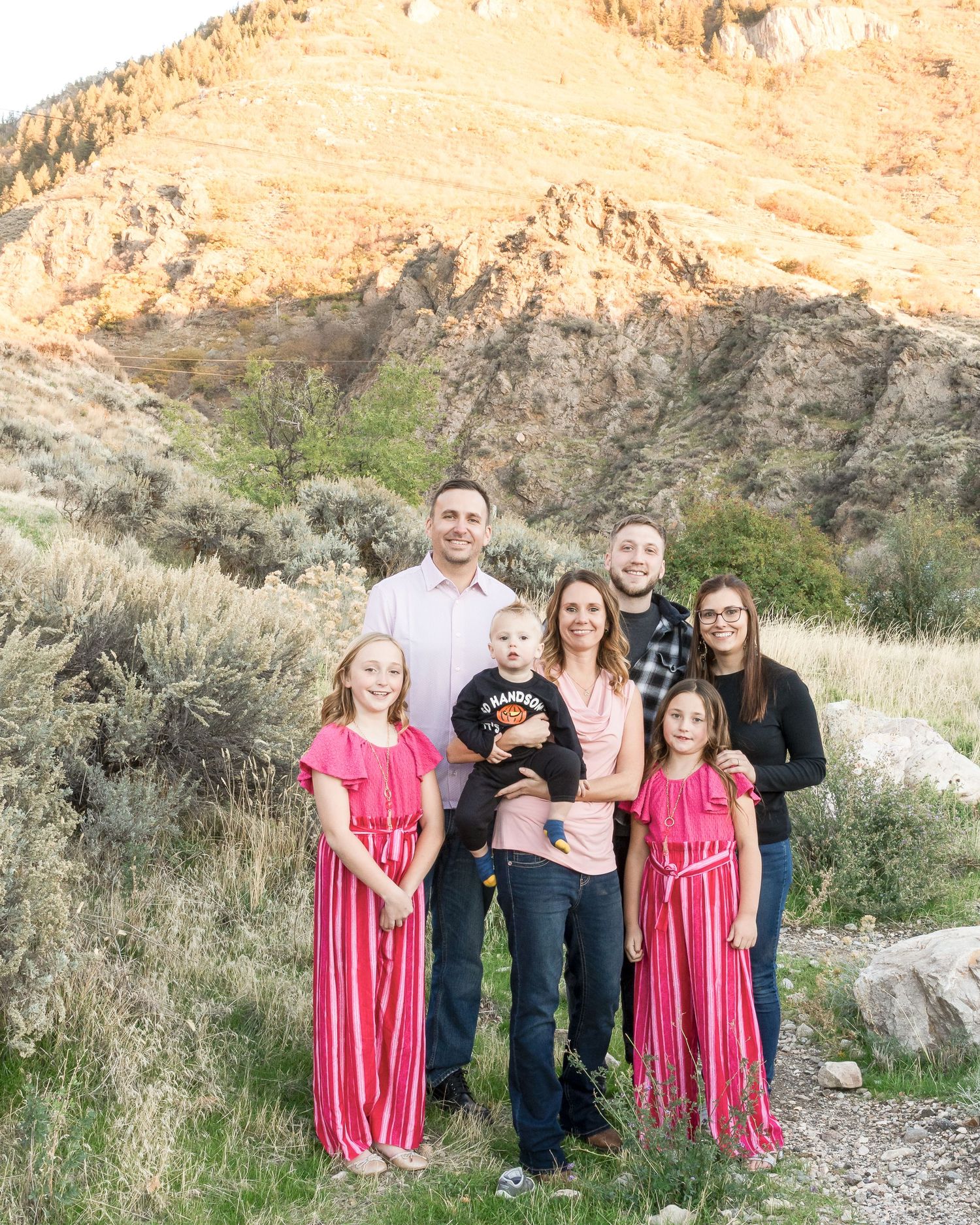 A family poses together against a scenic desert hillside backdrop with golden lighting and desert vegetation.