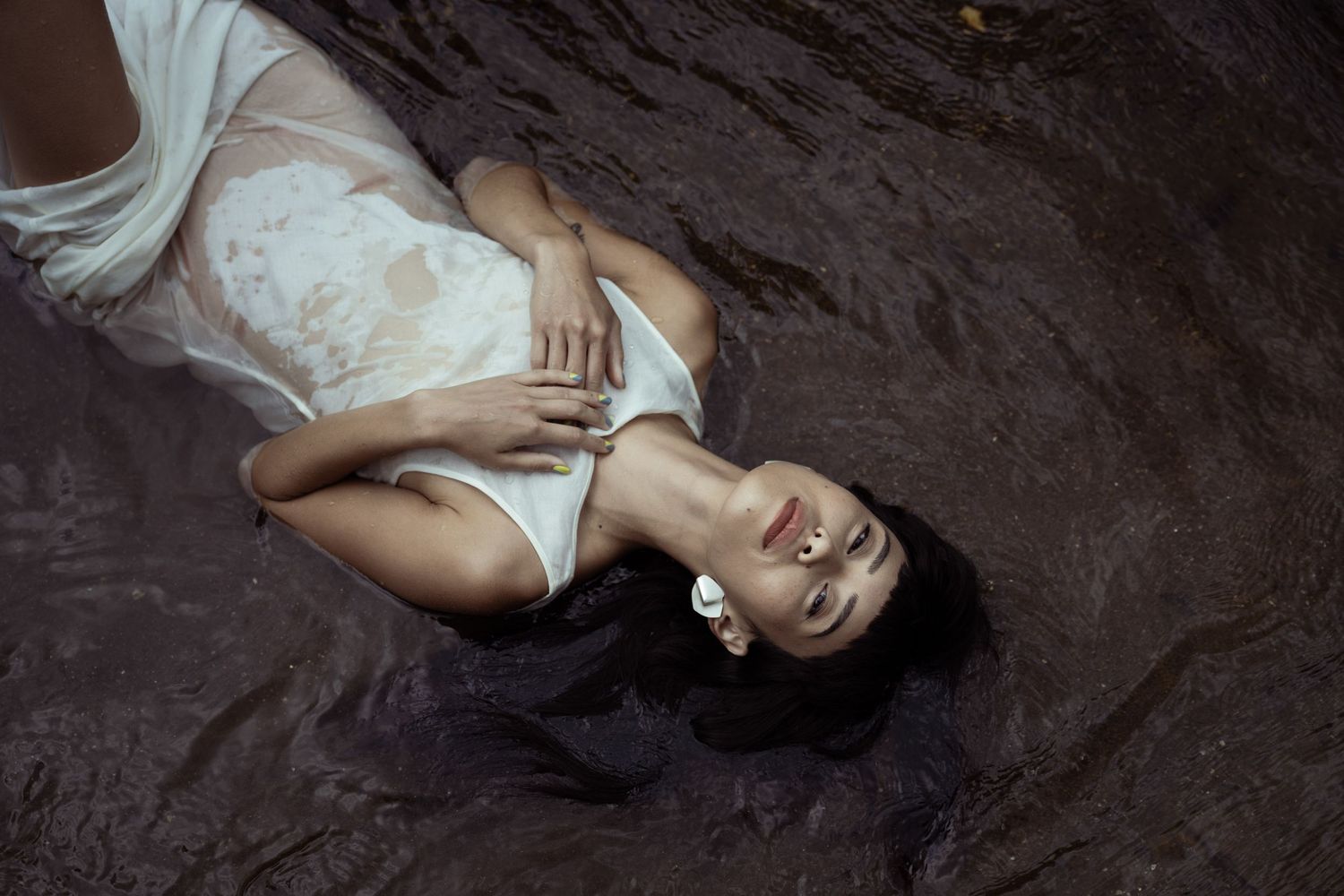 Atmospheric shot of a woman in a white slip dress lying on dark fabric; luxury hospitality branding and lifestyle content for Tuscany boutiq