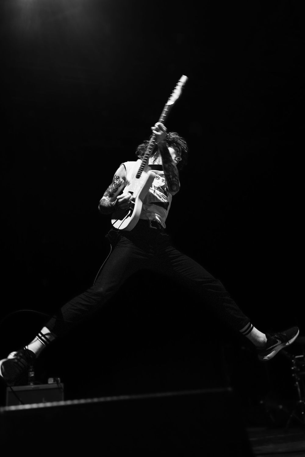 Black and white action shots of a performer jumping and playing guitar on stage during an energetic concert performance.