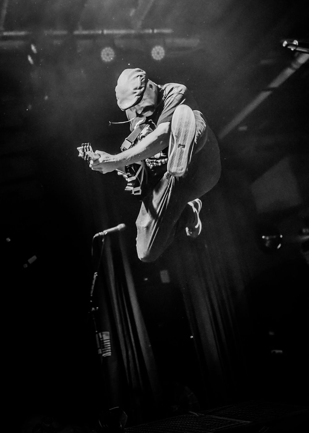 Dramatic black and white concert photo showing a performer jumping high in the air on stage during an energetic performance.