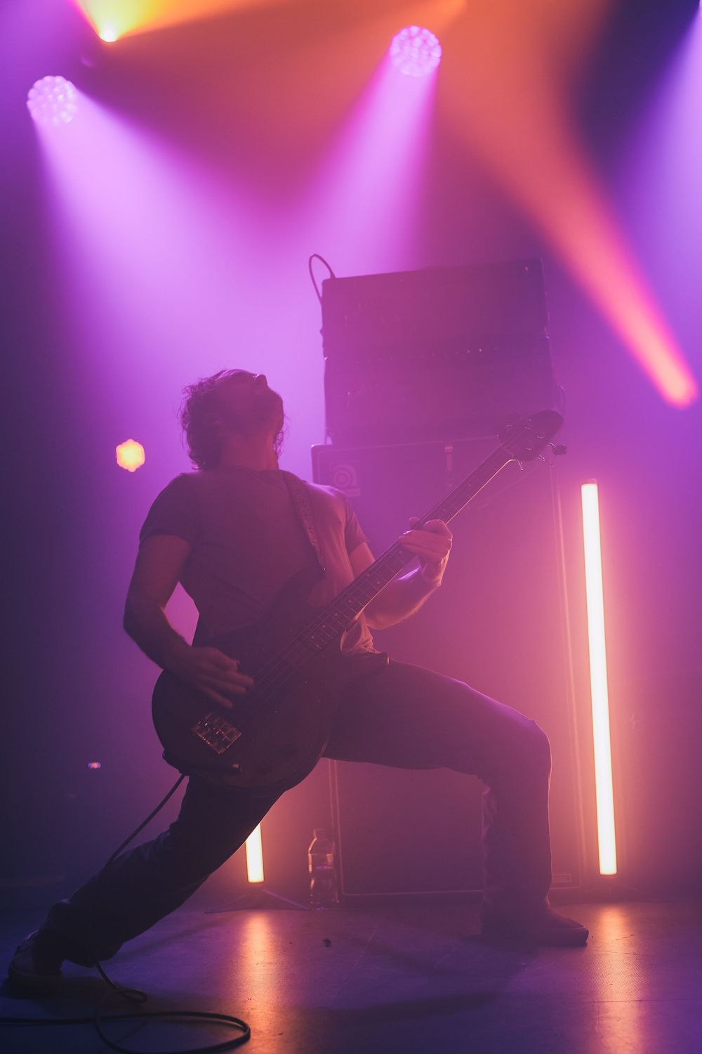 Silhouetted performers create dynamic poses in a purple-lit studio space with dramatic vertical light beams.