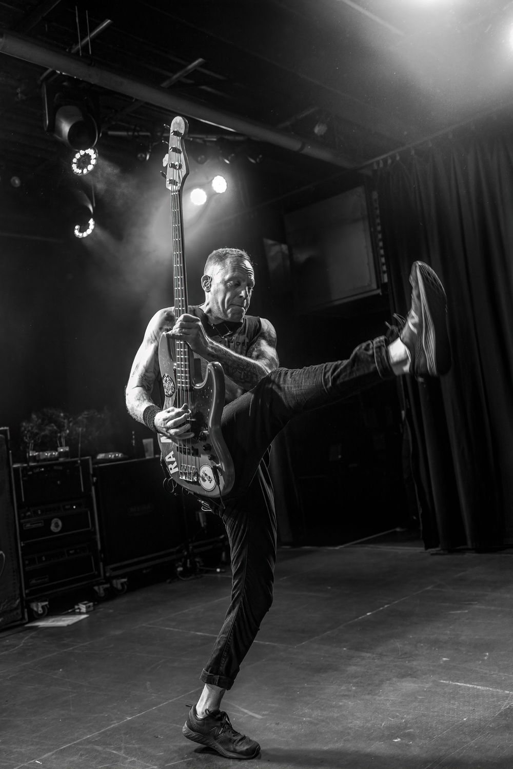 Black and white photos of a musician performing energetically with a bass guitar on a dark stage.