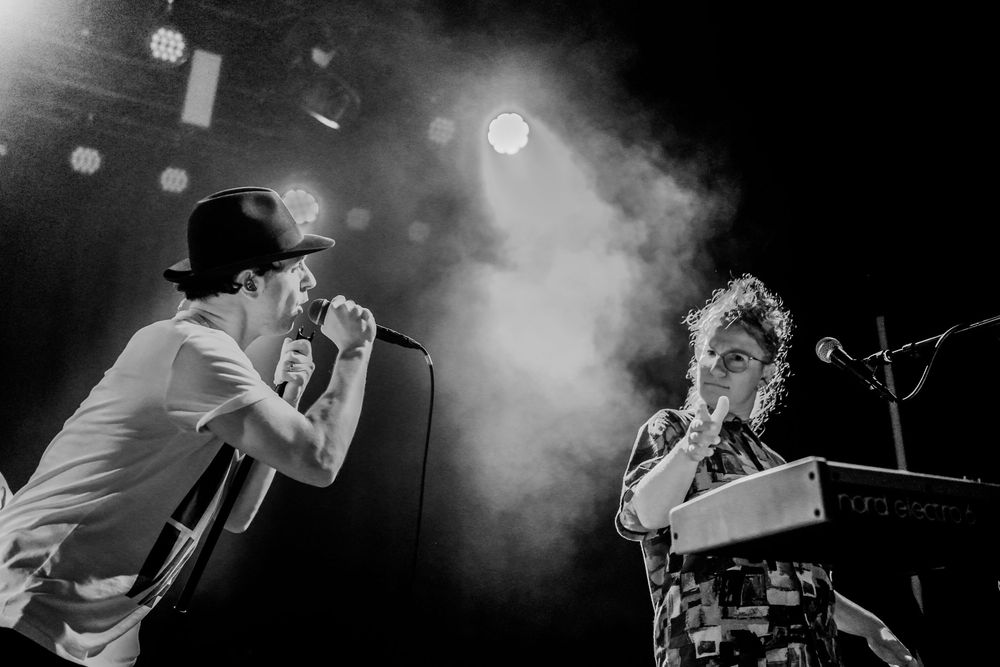 Atmospheric black and white concert performance with smoke effects and dramatic backlighting on stage.