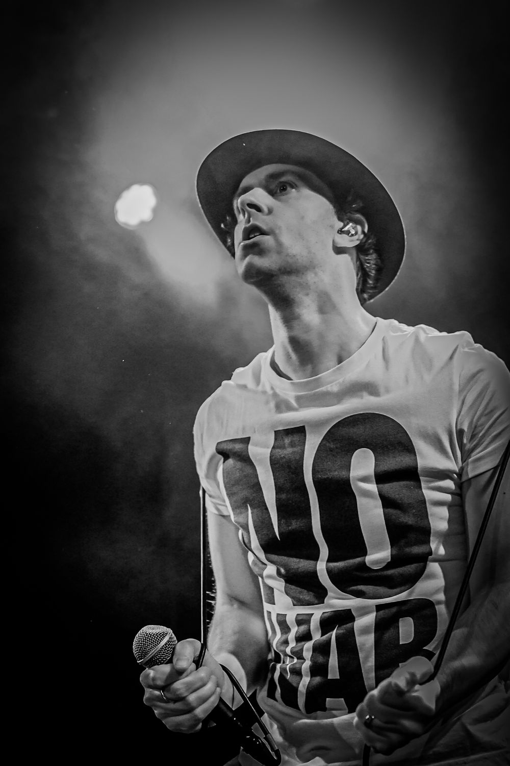 A black and white photo series of a performer in a baseball cap singing passionately into a microphone on stage.