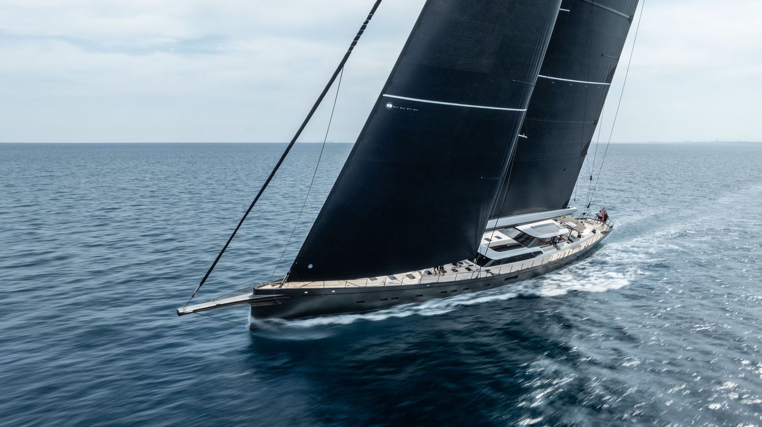 Modern racing yacht with large black sail cutting through calm blue waters.