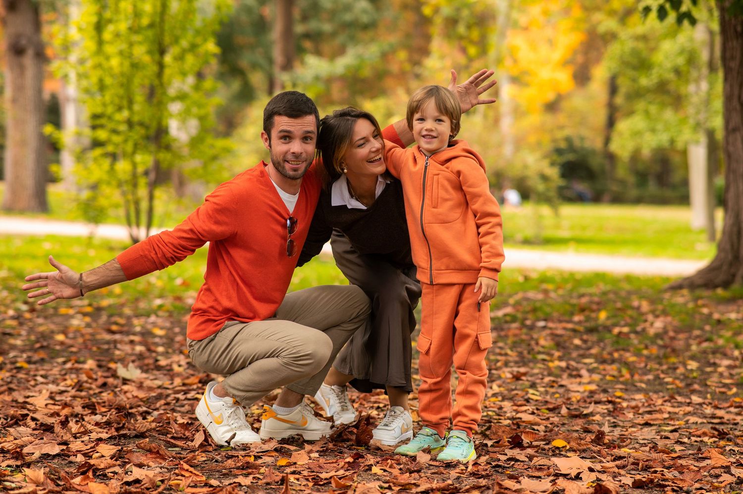 A family enjoys a playful moment together in a park filled with colorful autumn leaves on the ground.