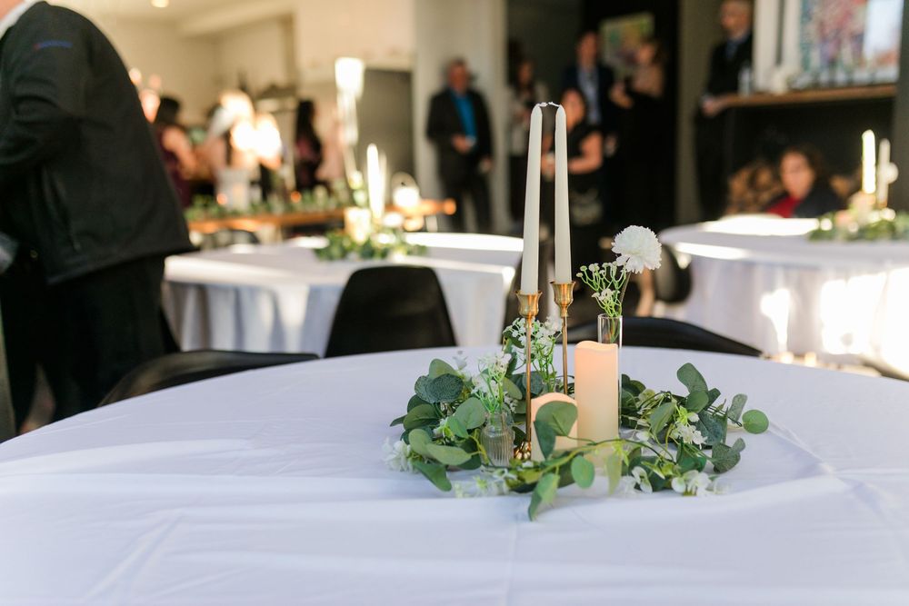 Elegant wedding reception tables decorated with white linens, greenery garlands, and glowing candlesticks in a banquet hall.