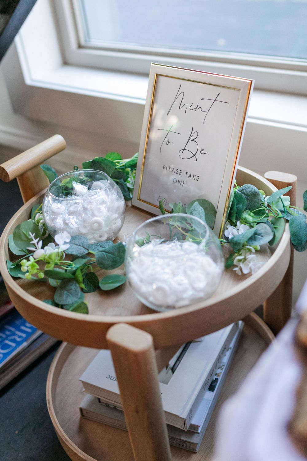 Wooden display table with small white gift boxes and greenery arranged for a wedding or event setup.