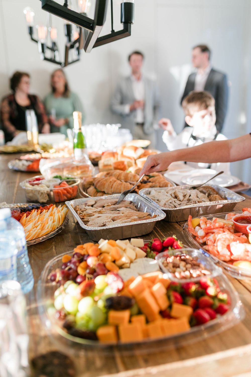 A catered buffet spread features fresh fruit, meats, and appetizers on wooden tables at a social gathering.