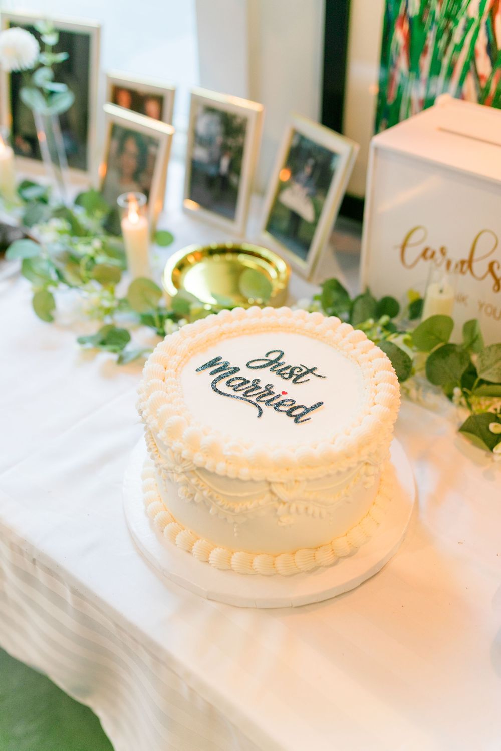 White frosted wedding cake with elegant piped decorations displayed on a light-colored tablecloth.