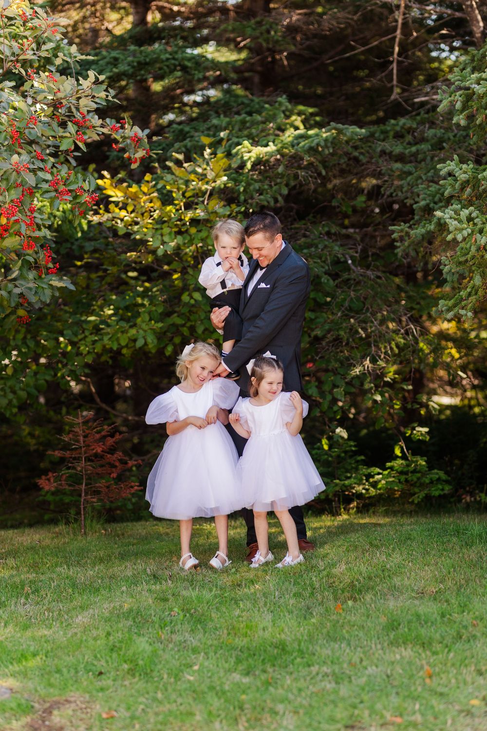 A family shares tender moments together outdoors on a grassy lawn surrounded by autumn foliage.