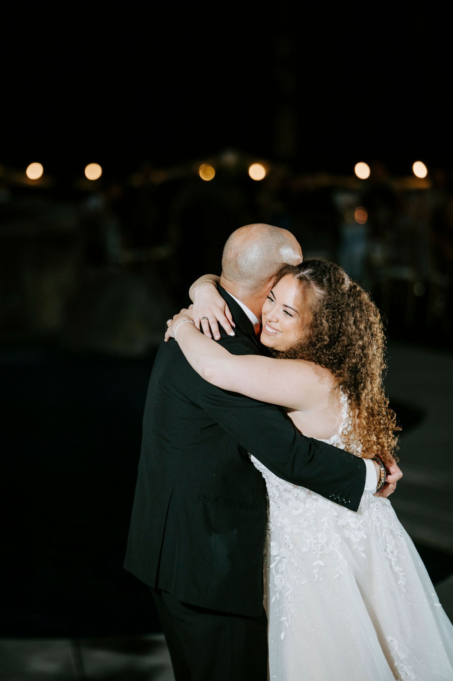 A couple shares an intimate dance moment at their wedding reception with twinkle lights in the background.