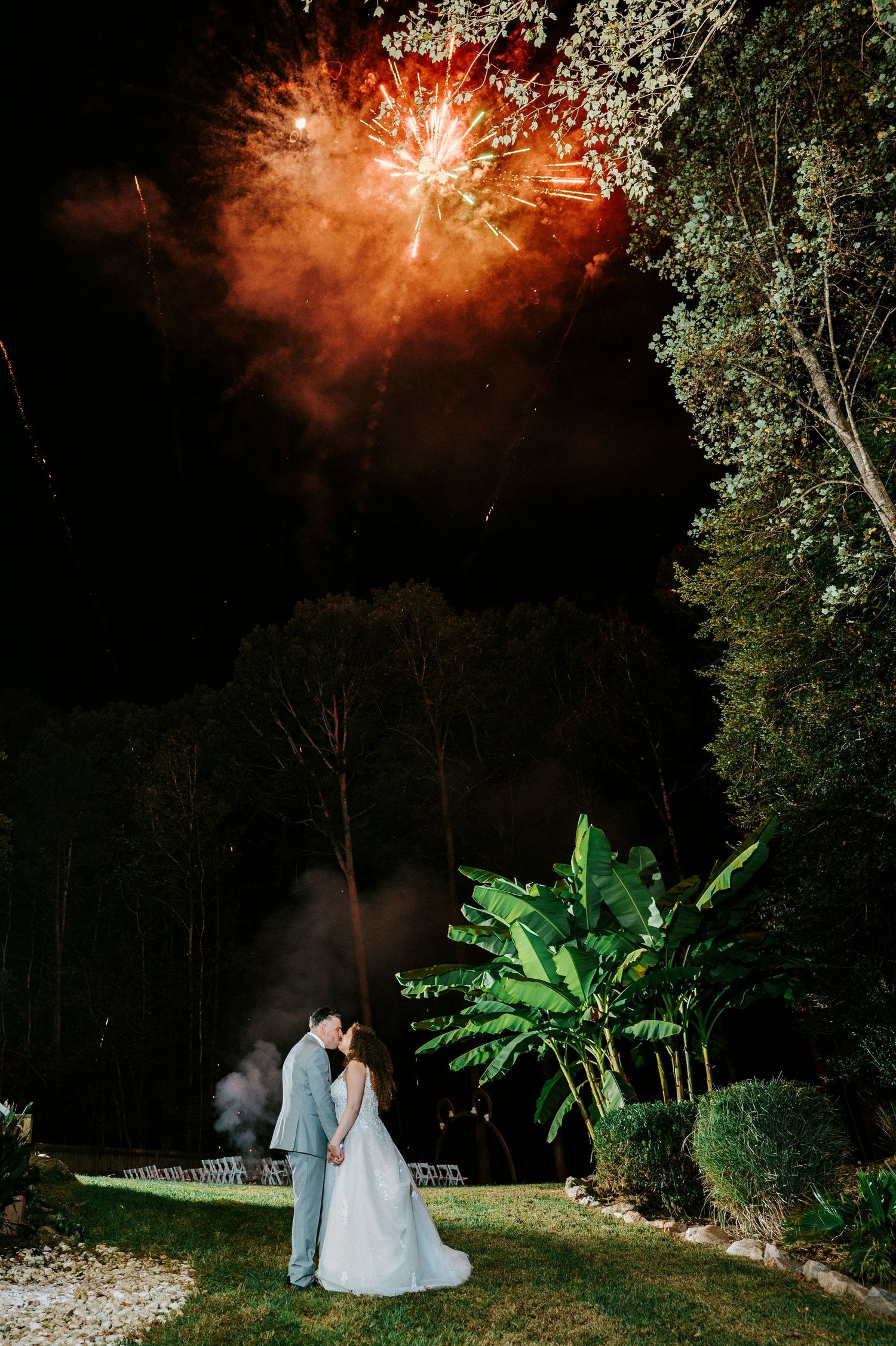 Couple enjoying a romantic moment under spectacular red fireworks display in a garden setting at night.