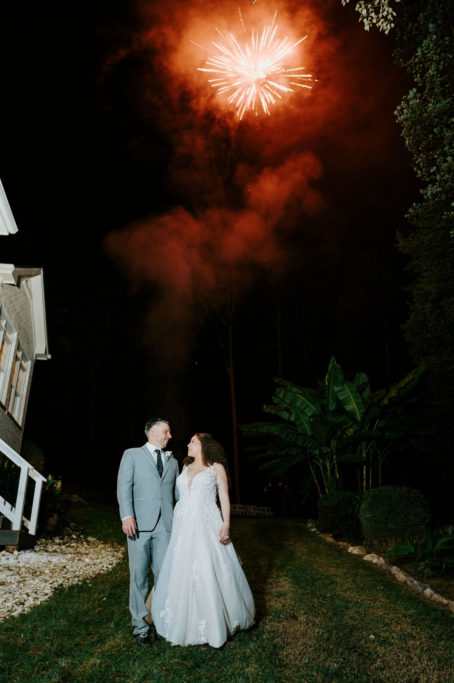 Fireworks illuminate the evening sky with a warm orange glow as silhouettes stand beneath the display.