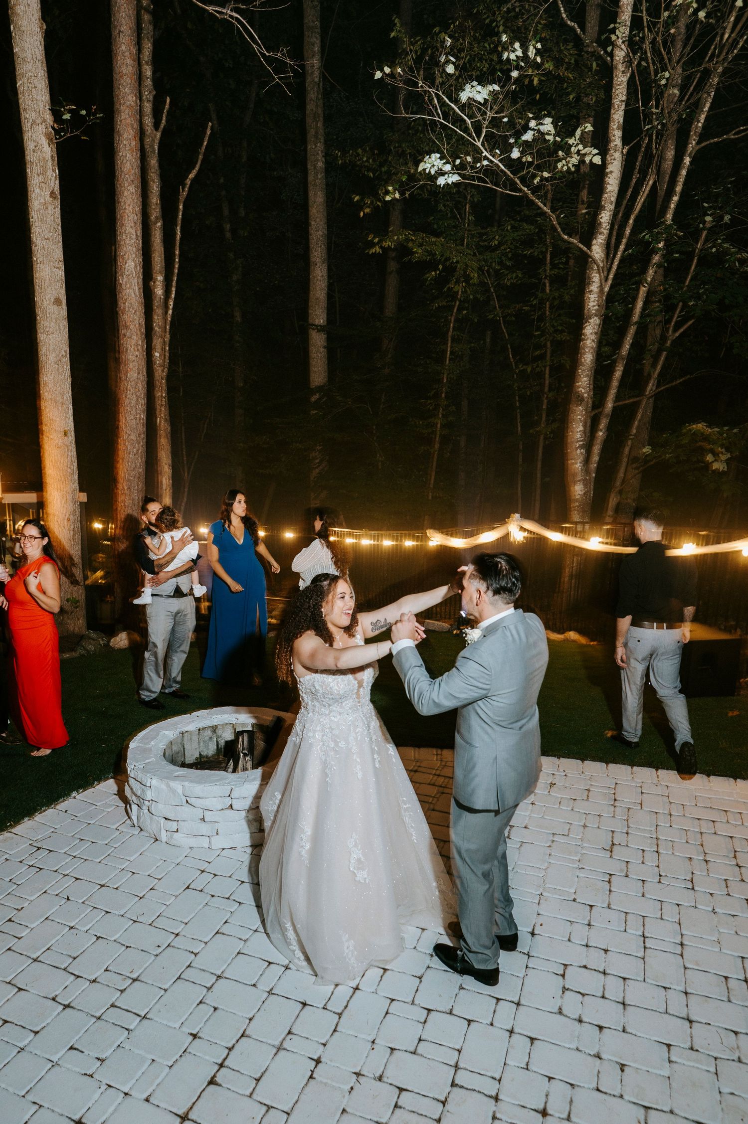 Wedding guests dancing on an illuminated outdoor stone patio at night.