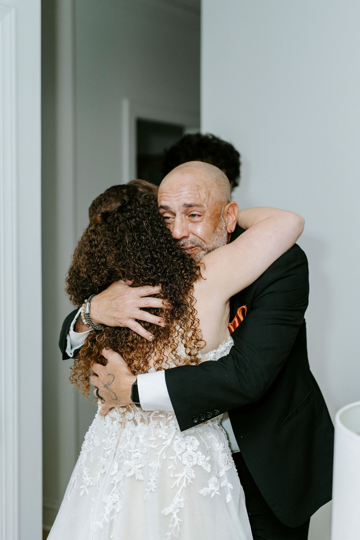 Emotional wedding moment captured in a series of intimate embraces against a white wall.