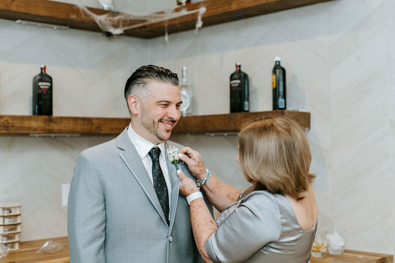 Wedding party members share joyful moments in a rustic indoor venue with wooden beams.