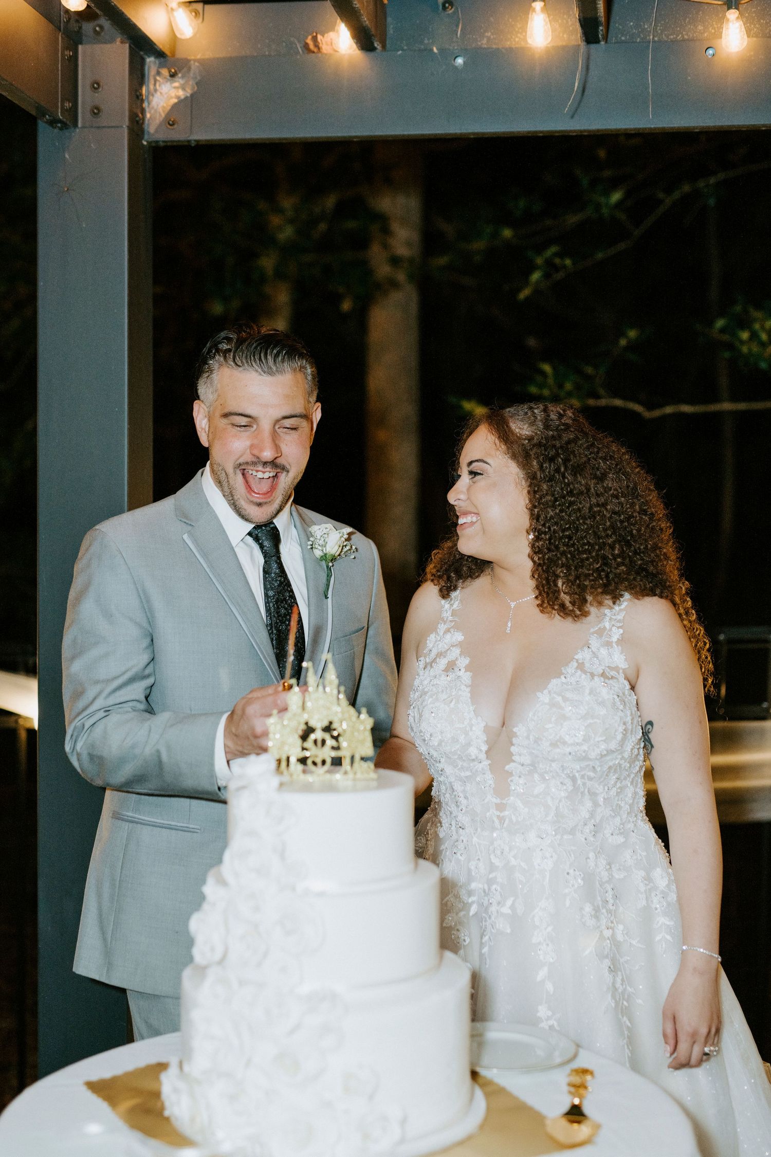 Newlyweds sharing a joyful moment while cutting their white tiered wedding cake.