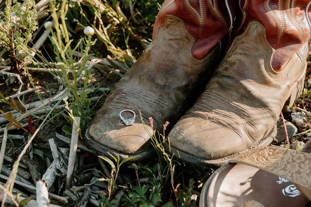 Worn leather boots with laces rest on grassy ground in natural outdoor lighting.