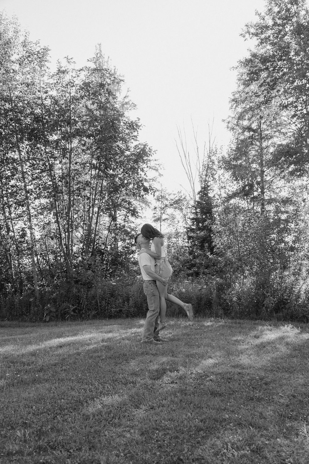 A sequence of black and white photos shows two people playing catch with a ball in a grassy field surrounded by trees.