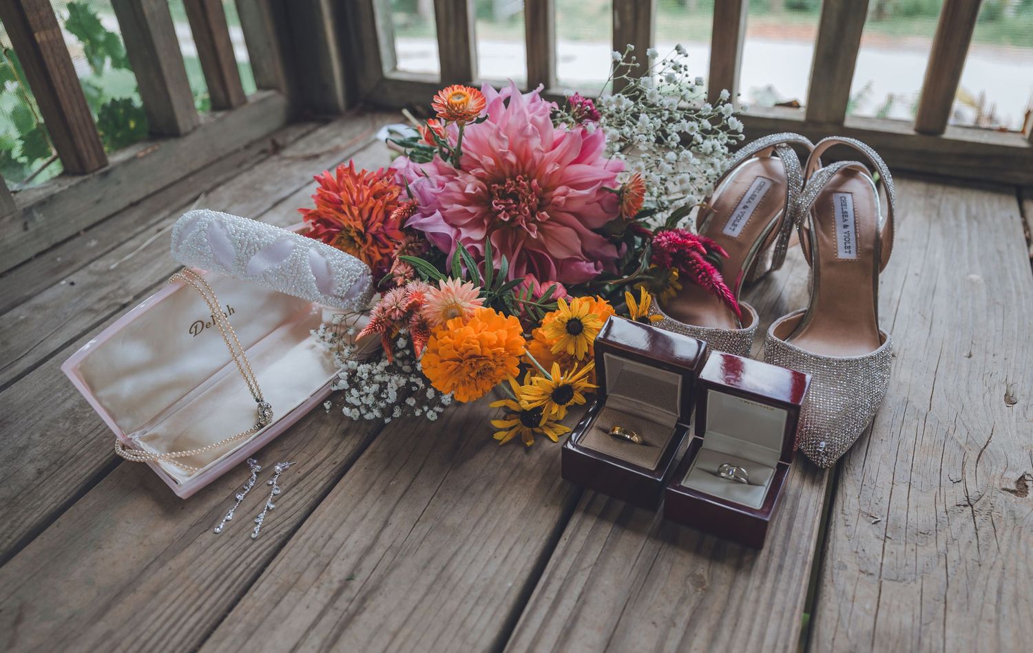 A series of floral arrangements in rustic vases line a wooden deck railing at sunset.